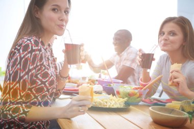 Ahşap masada otururken birlikte yemek yiyen bir grup insanın üst düzey görüntüsü. Masada yemek var. İnsanlar fast food yiyor..