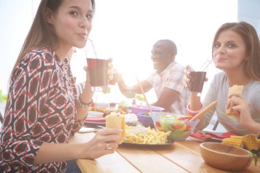 Ahşap masada otururken birlikte yemek yiyen bir grup insanın üst düzey görüntüsü. Masada yemek var. İnsanlar fast food yiyor..