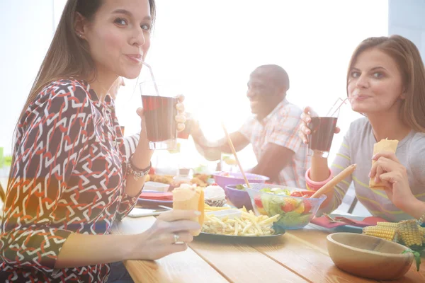 Ahşap masada otururken birlikte yemek yiyen bir grup insanın üst düzey görüntüsü. Masada yemek var. İnsanlar fast food yiyor..