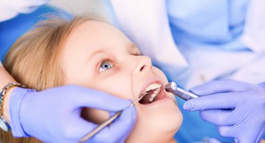 Küçük kız dişçi ofisinde oturuyor.