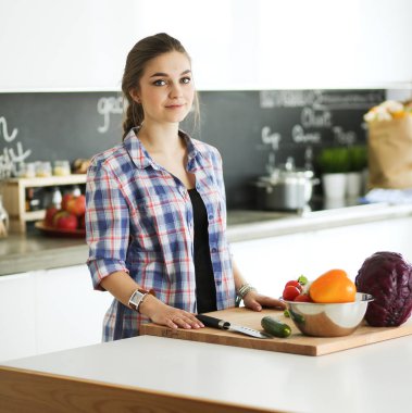 Masanın yanındaki mutfakta sebze doğrayan genç bir kadın..