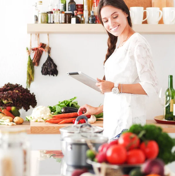 Jovem usando um computador tablet para cozinhar em sua cozinha. Jovem mulher — Fotografia de Stock