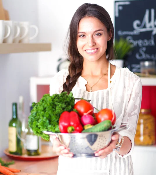 Улыбающаяся молодая женщина с овощами, стоящими на кухне. Улыбающаяся молодая женщина — стоковое фото