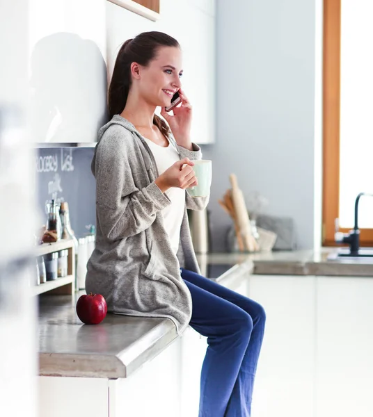 Kvinna med mobiltelefon sitter i moderna kök. — Stockfoto