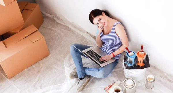 Yeni daire dizüstü bilgisayar ile oturup, boyama sırasında genç kadın portre. Dizüstü bilgisayar ile genç kadın