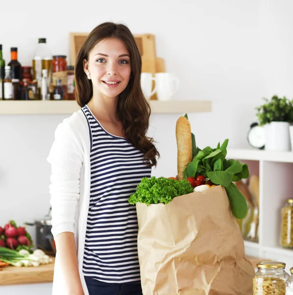 Bakkal alışveriş çantası sebzeli tutan genç kadın. Mutfakta ayakta. Genç kadın