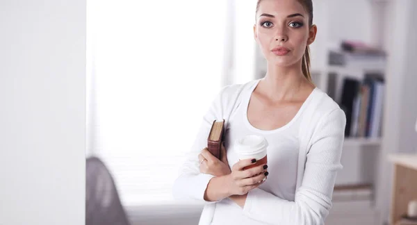 Attraktive Geschäftsfrau steht mit Buch an Wand im Büro. — Stockfoto