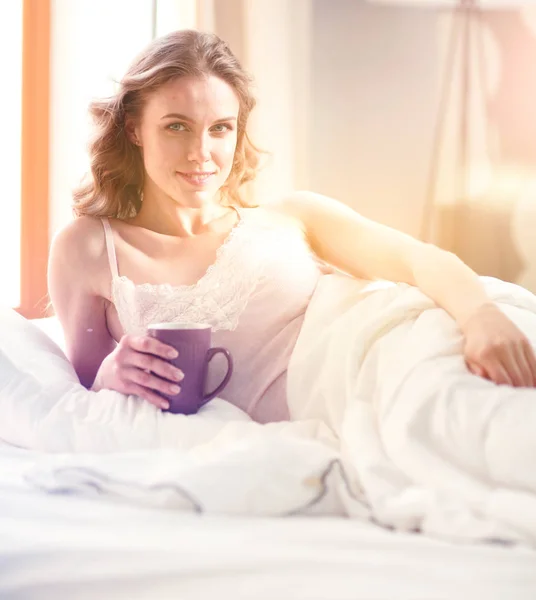 Young woman drinking cup of coffee or tea while lying in bed. — Stock Photo, Image