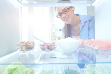 Sağlıklı yiyecek, sebze ve meyvelerle dolu açık buzdolabının yanında duran kadın portresi. Kadın portresi