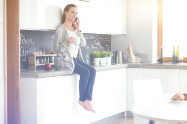 modern mutfakta otururken cep telefonu kullanan kadın.