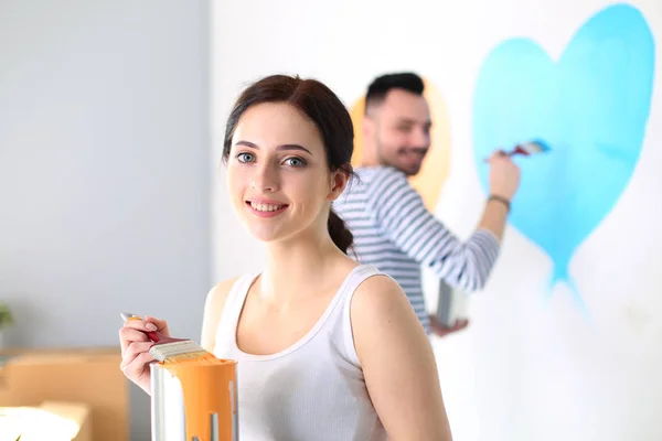 Ritratto di felice sorridente giovane coppia pittura parete interna della nuova casa. giovane coppia — Foto Stock