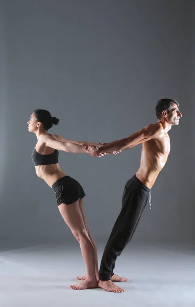 Casal jovem praticando acro ioga no tapete em estúdio juntos. Acroyoga. Um par de ioga. Parceiro ioga . — Fotografia de Stock