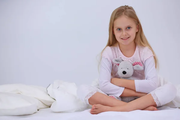 Liten flicka i sovrummet sitter på sängen. Lilla flickan bär en pyjamas och sitter i sängen . — Stockfoto