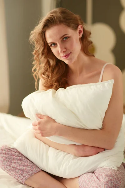 Young woman holding a pillow while sitting on her bed. — Stock Photo, Image