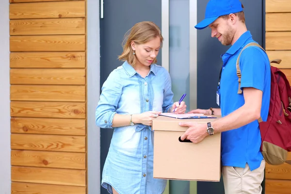 Repartidor sonriente con uniforme azul que entrega la caja de paquetes al destinatario: concepto de servicio de mensajería. Repartidor sonriente en uniforme azul — Foto de Stock