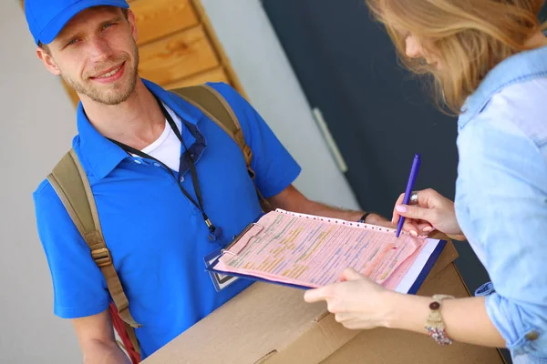 Mavi üniformalı gülümseyen kurye servis konseptine paket kutusu teslim eden teslimatçı. Mavi üniformalı gülümseyen teslimatçı.