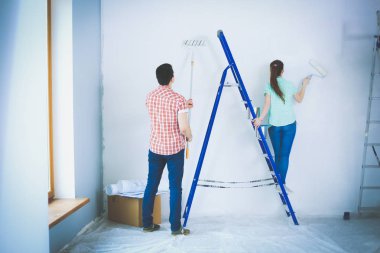 Yeni evin içini boyayan mutlu, gülümseyen genç bir çift portresi. Genç çift