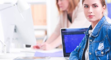 İki genç kadın masada enstrümanlar, planlar ve dizüstü bilgisayarlarla oturuyor.