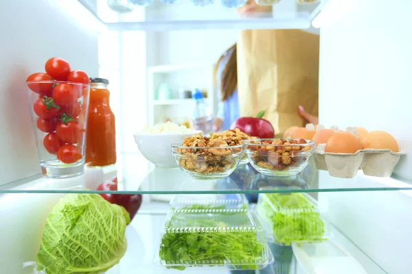 Retrato de una mujer parada cerca de una nevera abierta llena de alimentos saludables, verduras y frutas. Retrato de mujer — Foto de Stock