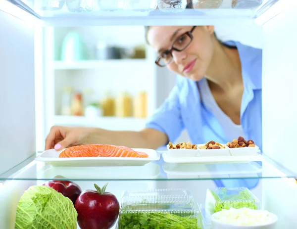 Sağlıklı yiyecek, sebze ve meyvelerle dolu açık buzdolabının yanında duran kadın portresi. Kadın portresi