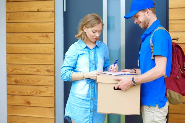 Repartidor sonriente con uniforme azul que entrega la caja de paquetes al destinatario: concepto de servicio de mensajería. Repartidor sonriente en uniforme azul — Foto de Stock