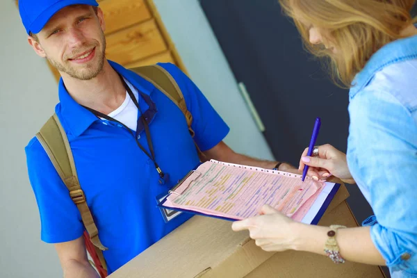 Repartidor sonriente con uniforme azul que entrega la caja de paquetes al destinatario: concepto de servicio de mensajería. Repartidor sonriente en uniforme azul — Foto de Stock