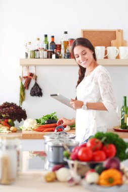 Mutfağında yemek için bir tablet bilgisayar kullanan genç kadın. Genç kadın