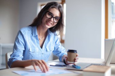 Ofis masasında oturan genç bir kadın dizüstü bilgisayar ekranına bakıyor. Genç kadın.