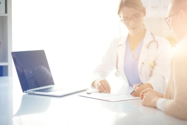 Arzt und Patient diskutieren etwas, am Schreibtisch sitzend. — Stockfoto
