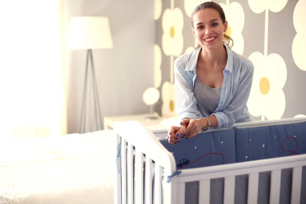 Jonge vrouw stond in de buurt van childrens kinderbed. Jonge moeder — Stockfoto