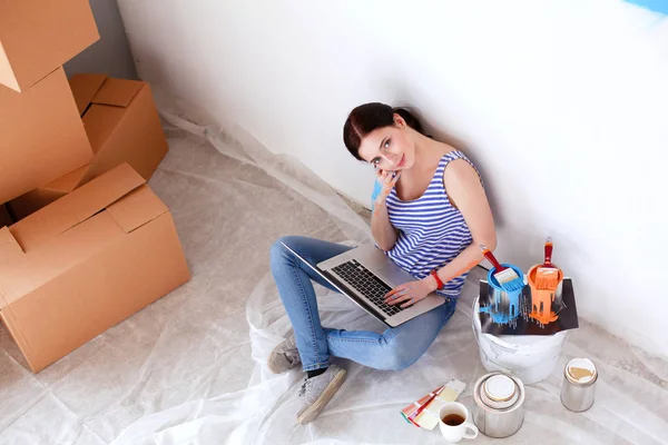 Portret van de jonge vrouw tijdens het schilderen van nieuw appartement, zitten met laptop. Jonge vrouw met laptop — Stockfoto