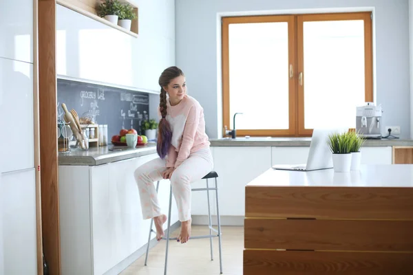 Jovem mulher sentada na mesa na cozinha . — Fotografia de Stock