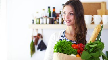 Bakkal alışveriş çantası sebzeli tutan genç kadın. Mutfakta ayakta. Genç kadın