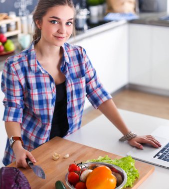 Masanın yanındaki mutfakta sebze doğrayan genç bir kadın..