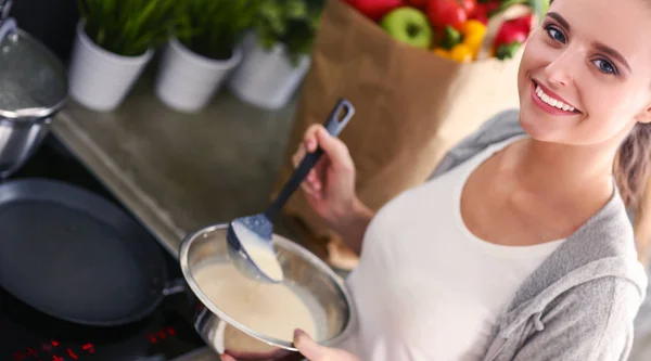 Mujer joven prepara panqueques en la cocina mientras está de pie cerca de la mesa. Mujer en la cocina. Cocinar en la cocina. —  Fotos de Stock