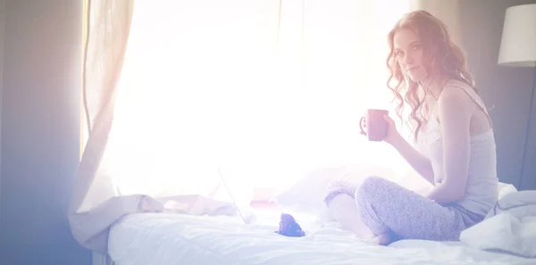 Jovem bela mulher sentada na cama com laptop . — Fotografia de Stock