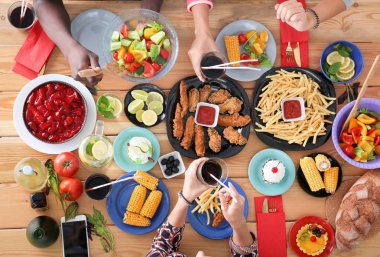 Ahşap masada otururken birlikte yemek yiyen bir grup insanın üst düzey görüntüsü. Masada yemek var. İnsanlar fast food yiyor..