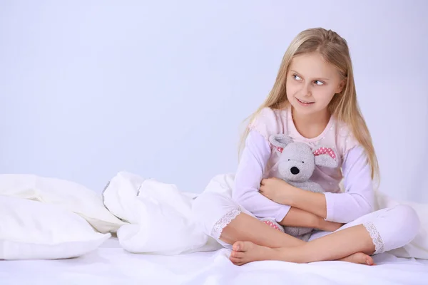 Little girl in the bedroom is sitting on the bed. Little girl is wearing a pajamas and sitting in bed . — Stock Photo, Image