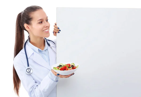 Portrait of a beautiful woman doctor holding a plate with fresh vegetables standing near blank. Woman doctors — Stock Photo, Image