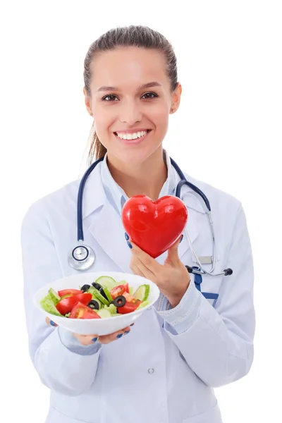 Retrato de una hermosa doctora sosteniendo un plato con vegetales frescos y corazón rojo. Mujeres doctores . — Foto de Stock