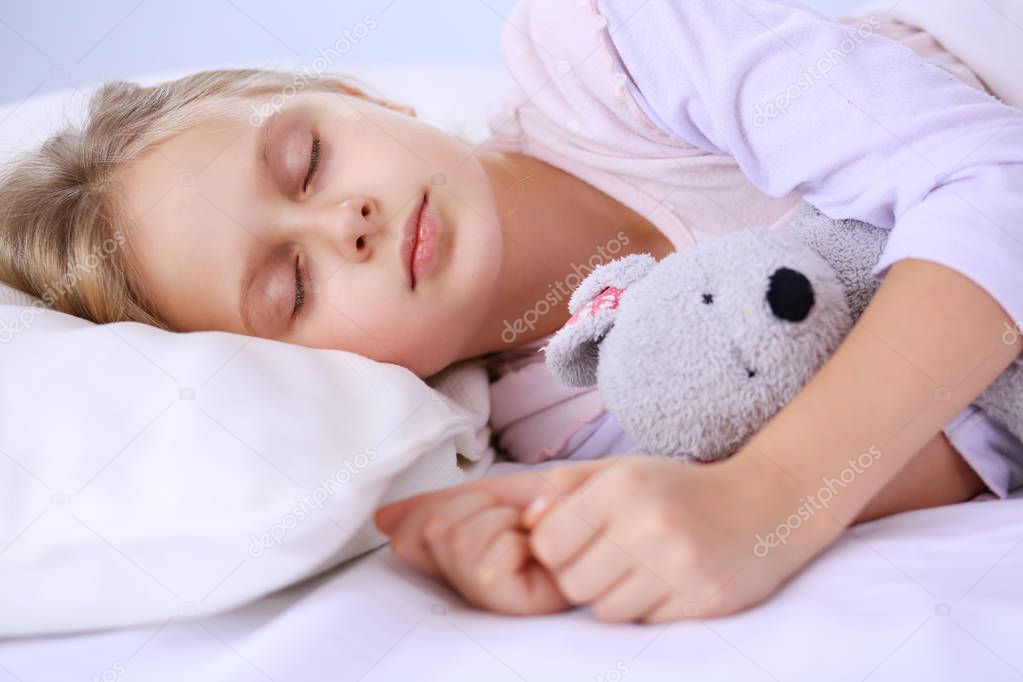 Child little girl sleeps in the bed with a toy teddy bear.