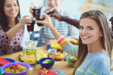 Ahşap masada otururken birlikte yemek yiyen bir grup insanın üst düzey görüntüsü. Masada yemek var. İnsanlar fast food yiyor. Bir kızın portresi.