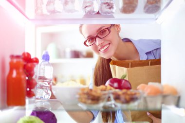 Sağlıklı yiyecek, sebze ve meyvelerle dolu açık buzdolabının yanında duran kadın portresi..