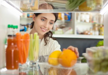 Sağlıklı yiyecek, sebze ve meyvelerle dolu açık buzdolabının yanında duran kadın portresi. Kadın portresi