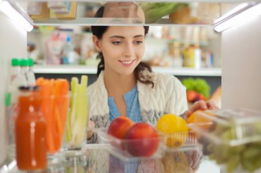 Sağlıklı yiyecek, sebze ve meyvelerle dolu açık buzdolabının yanında duran kadın portresi. Kadın portresi