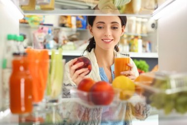 Sağlıklı yiyecek, sebze ve meyvelerle dolu açık buzdolabının yanında duran kadın portresi. Kadın portresi