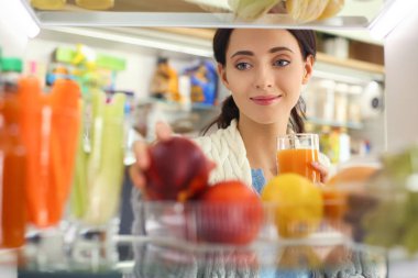 Sağlıklı yiyecek, sebze ve meyvelerle dolu açık buzdolabının yanında duran kadın portresi. Kadın portresi