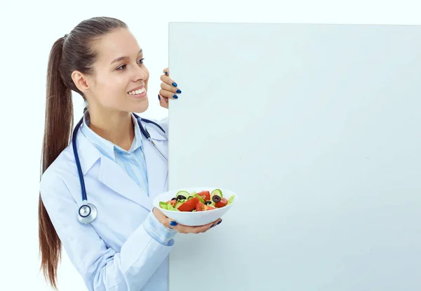 Retrato de uma mulher bonita médico segurando um prato com legumes frescos em pé perto de branco. Mulheres médicas — Fotografia de Stock