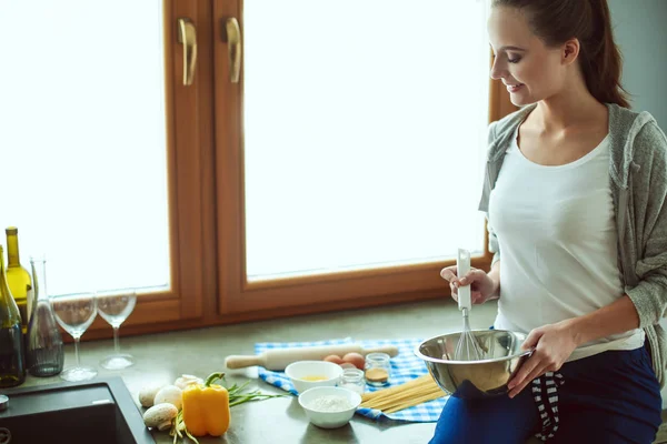 Jovem prepara panquecas na cozinha enquanto está perto da mesa. Uma mulher na cozinha. Cozinhar na cozinha. — Fotografia de Stock