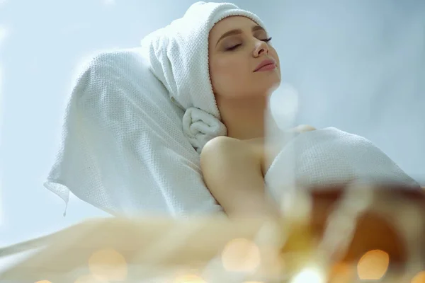 Mujer joven acostada en una mesa de masaje, relajándose con los ojos cerrados. Una mujer. Salón de spa — Foto de Stock